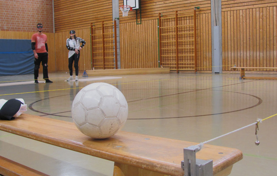 Ein Torball liegt auf einer Bank. Daneben sind die gelben Leinen gespannt und ein Glöckchen daran zu sehen