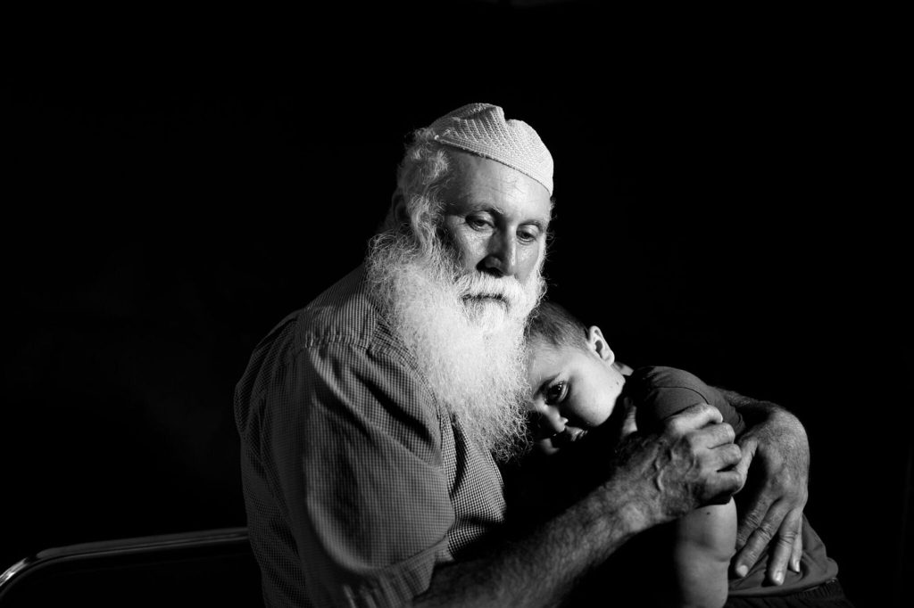 Alter Mann mit Kappe und weißem Bart hält Kind im Arm
