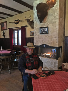 Mann mit grauem Schnurrbart im Cowboy-Outfit sitzt vor Kamin in einem originalgetreuen Western-Saloon