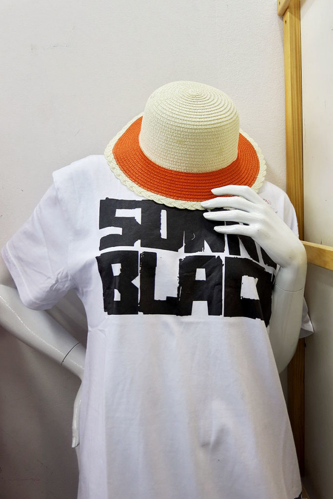 Eine Schaufensterpuppe trägt ein weißes T-Shirt mit schwarzer Schrift und einen weißen Strohut mit oranger Krempe