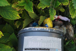 Eimer Wandfarbe liegt im Grünen, Müll drum herum