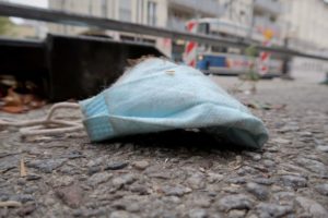 Corona-Maske liegt in der Stadt auf dem Boden, im Hintergrund die Münchner Tram