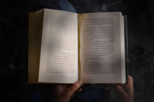 Blick auf ein geöffnetes Buch in einem Schoß, dass von zwei Händen gehalten wird. Es hat bereits ein leichter Tunnelblick eingesetzt. Foto: Jonas Kessel