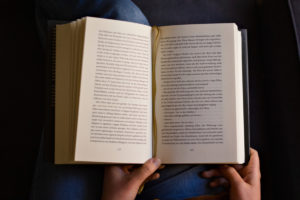 Blick auf ein geöffnetes Buch in einem Schoß, dass von zwei Händen gehalten wird. Foto: Jonas Kessel