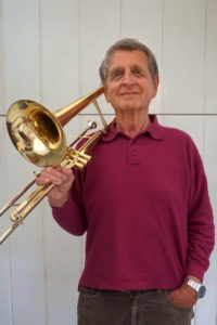 Werner Riedel trägt einen violetten Pullover und hat lässg sein Instrument die Tenorpsaune geschultert. Foto: Nina Jarosch