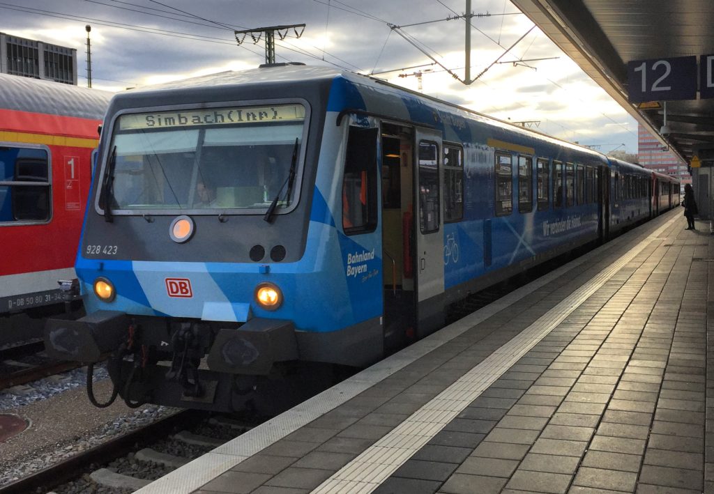Ein Zug mit einer blauen Lackierung steht am Gleis 12 im Hintergrund graue Wolken und Sonne