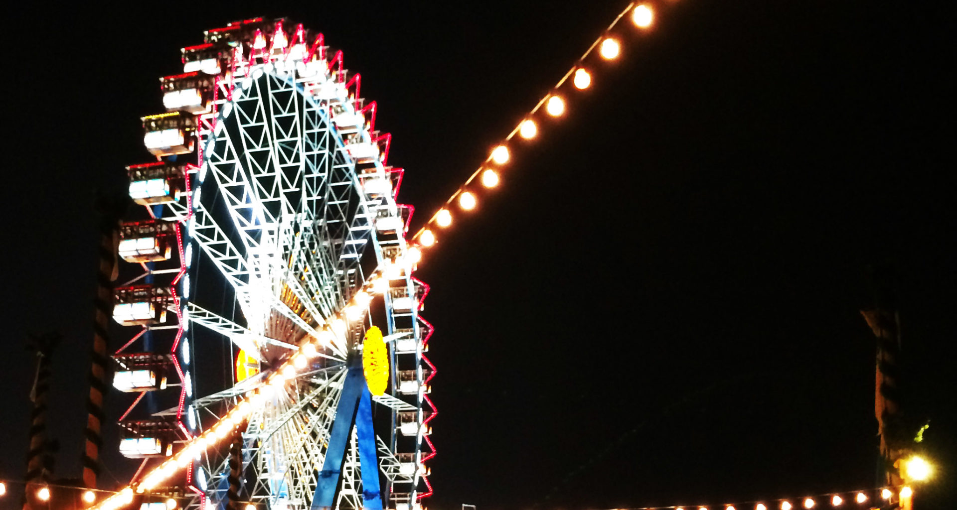 Bunt erleuchtetes Riesenrad und Lichtergirlanden vor schwarzem Nachthimmel