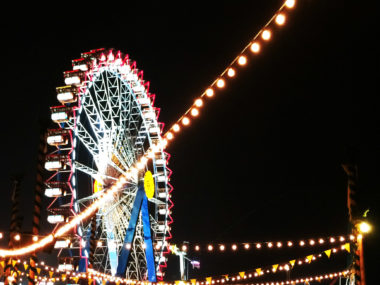 Bunt erleuchtetes Riesenrad und Lichtergirlanden vor schwarzem Nachthimmel