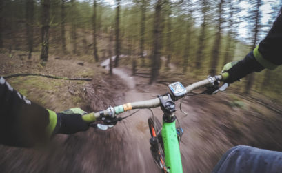 Ein Mountainbiker fährt auf einem Trail durch den Wald. Das Foto ist aus der Perspektive des fahrenden Mountainbiker aufgenommen.rs