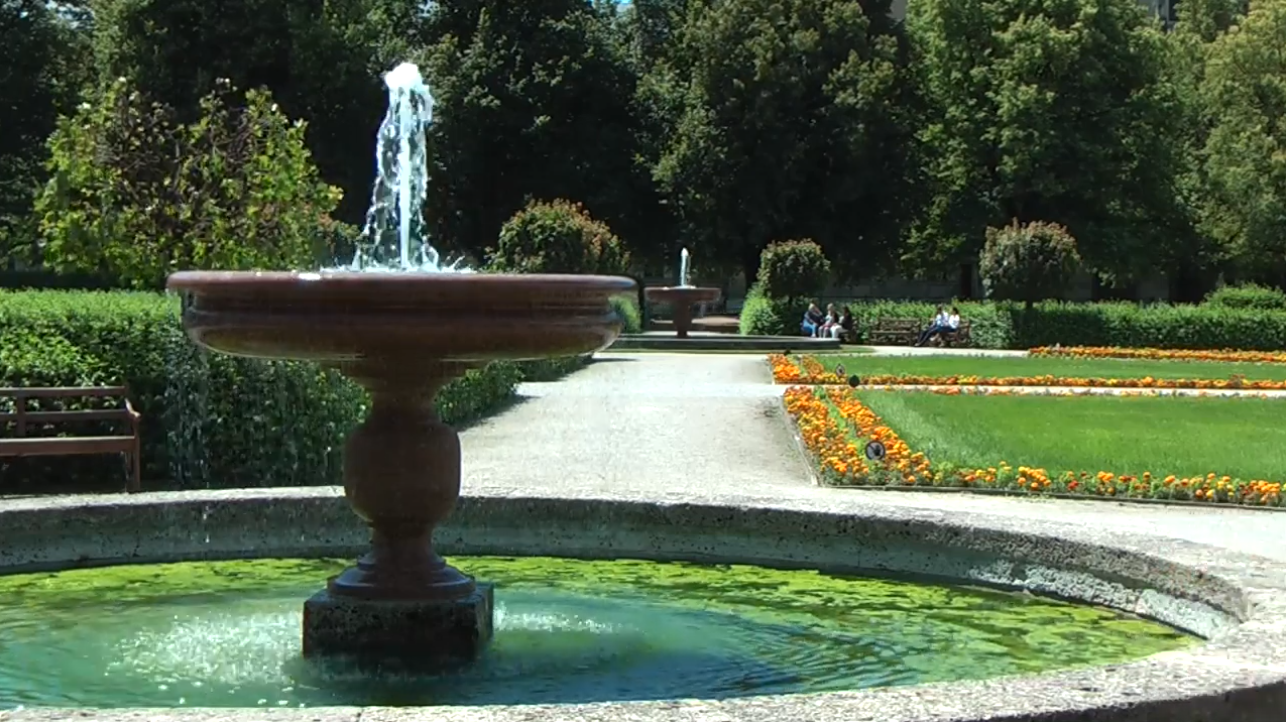 Zwei Brunnen verbunden durch einen Weg, dazwischen sind Blumenbeete, Rasenflächen und Hecken zu sehen.